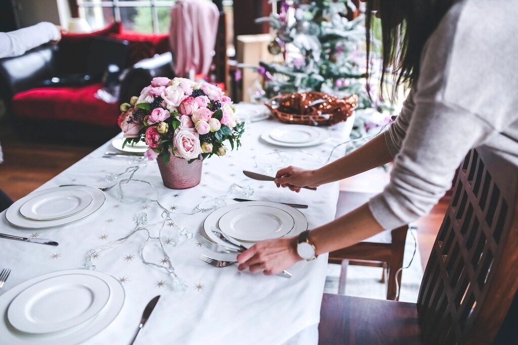 Une personne dispose les couverts sur une table nappée de blanc.