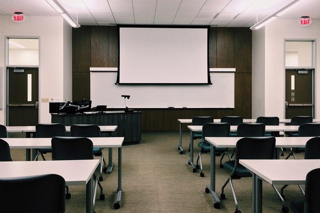 Salle de cours avec des tables, des chaises et un écran de projection.