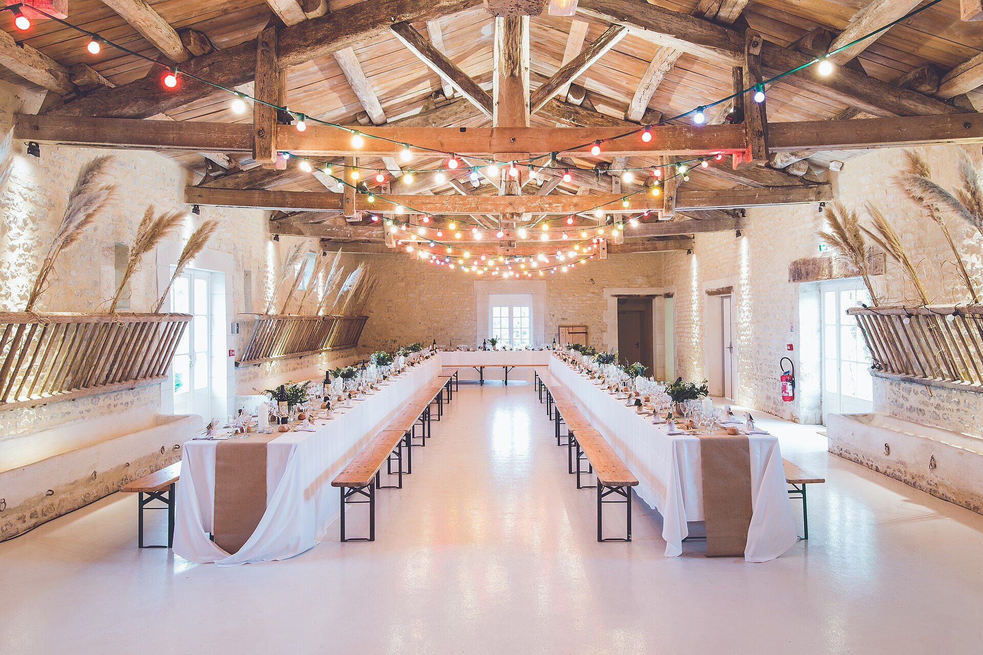 Grande salle de réception aux longues tables dressées, sous une charpente éclairée.