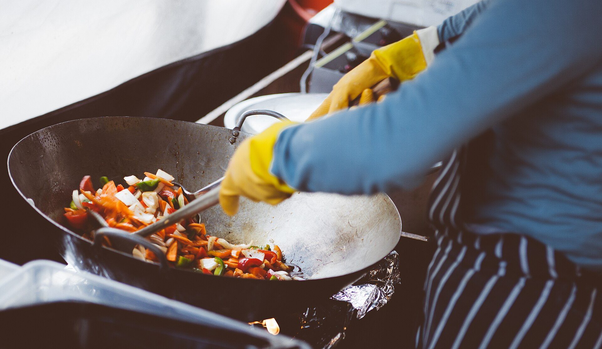 Un cuisinier ganté fait sauter des légumes à la poêle.