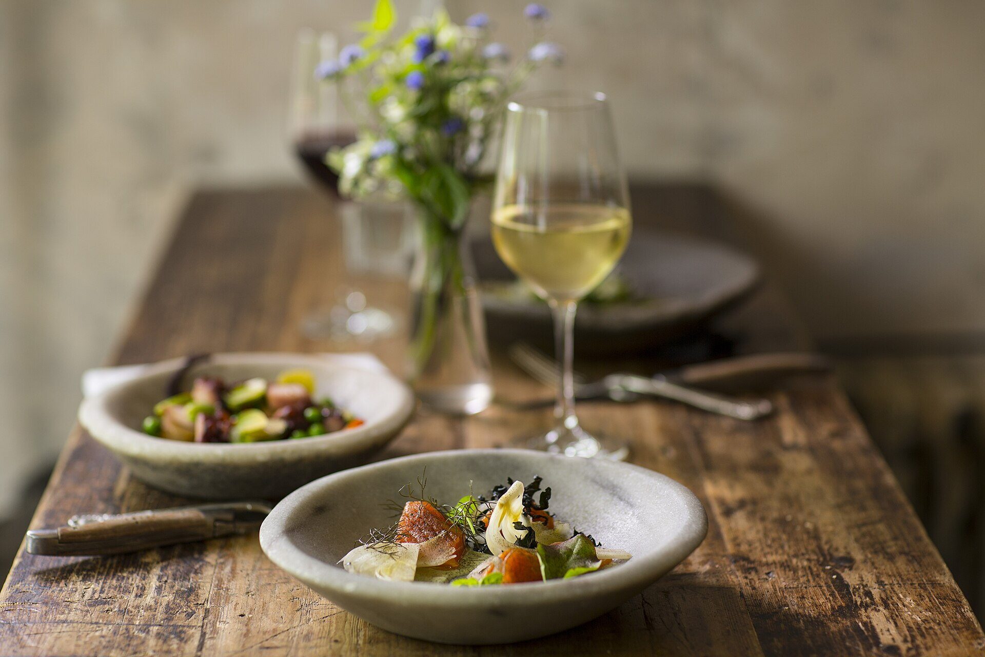 Table en bois dressée avec deux assiettes et un verre de vin blanc.